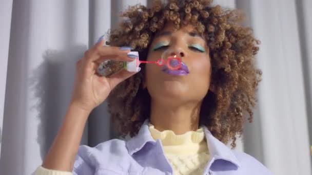 Blandad ras kvinna på grå gardiner bakgrund i pastell färger kläder dans och blåser till en bubbla fläkt — Stockvideo