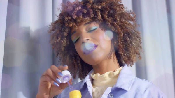 Черная женщина смешанной расы с кудрявыми волосами в пастельных тонах с пузырьками и блестящим макияжем — стоковое фото