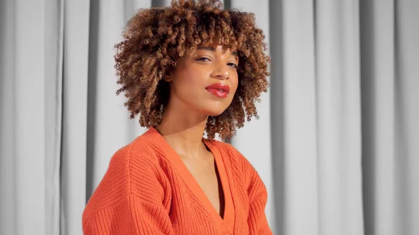 Gemengde race zwart volwassen vrouw portret op grijze gordijnen in fel oranje gebreide jas — Stockfoto