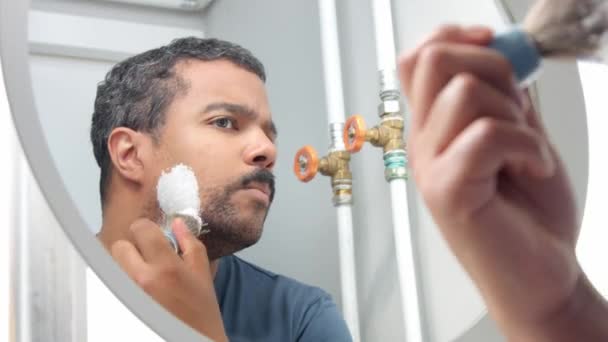 Человек за зеркалом надел пену для бритья — стоковое видео