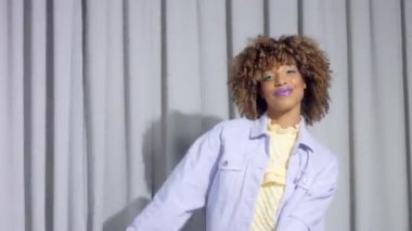 Gri perdelerdeki melez kadın pastel renklerde arka planda dans ediyor ve eğleniyor.