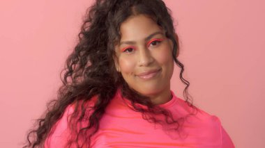 Pembe stüdyodaki genç kadın neon balıkçı yaka ve neon makyaj giyiyor.