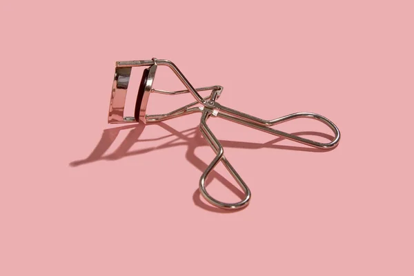 Um curler de pestanas em fundo rosa — Fotografia de Stock