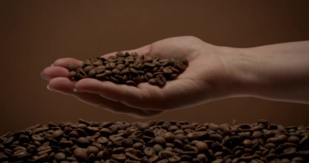weibliche Hand voller Kaffeebohnen dreht sich und Kaffeebohnen fallen langsam herunter