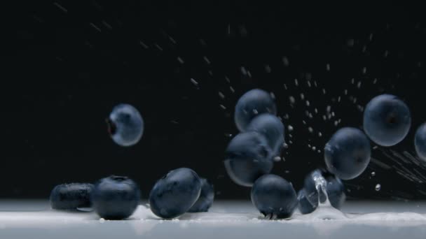 Vista lateral close-up de mirtilo caindo para a mesa com salpicos de água — Vídeo de Stock