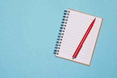 Üstten Görünüm boş spiral defter ve kırmızı kalem mavi pastel renk arka plan boşluk üzerinde. Fikir ve ilham renkli arka plan üzerinde boş yazı defteri