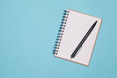  Top görünümünde boş spiral defter ve alanı olan mavi pastel renk arka plan üzerinde siyah kalem. Fikir ve ilham renkli arka plan üzerinde boş yazı defteri
