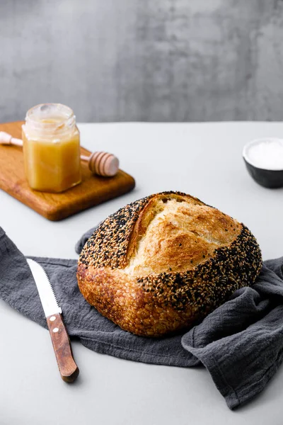 Round loaf of freshly baked sourdough bread with knife on cutting board. Artisan bread with seeds on dark table. Rustic sourdough bread.