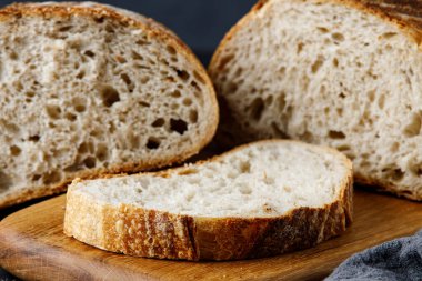Geleneksel buğday taze kırsal ekmek, tahta kesim tahtası ve havluyla dilimlenmiş. Bıçaklı ekşi ekmek.. 