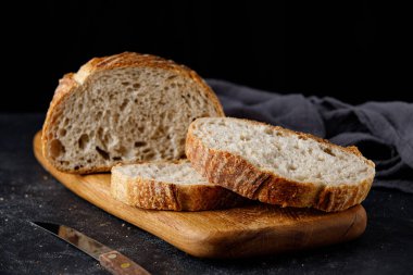 Geleneksel buğday taze kırsal ekmek, tahta kesim tahtası ve havluyla dilimlenmiş. Bıçaklı ekşi ekmek.. 