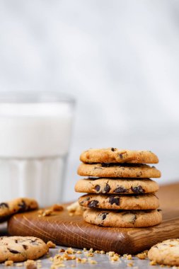 Tahta kesme tahtasında bir yığın çikolatalı kurabiye ve mermer masada bir bardak süt. Metin için boş yeri olan beyaz arkaplan