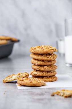 Beyaz parşömen üzerinde bir yığın fıstık kurabiyesi ve beton arka planda bir bardak süt.