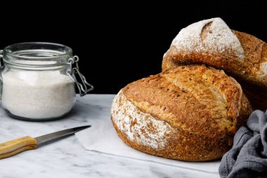 İki kırsal buğday ekmeği ve mermer bir arka planda keten. Ekşi ekmek ve bir kavanoz un.
