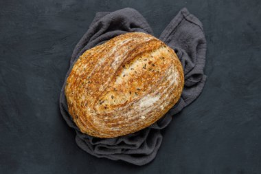 Havlunun üstünde fırında pişmiş taze ekmek. Karanlık masa üzerinde tohumlu zanaatkar ekmeği. Kırsal ekşi ekmek, üst manzara..