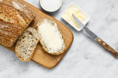 Peçetede ekmek ve tereyağı, üst manzara. Kahvaltıda taze ekmek ve organik tereyağı. Beyaz mermer masa üzerinde kırsal ekşi ekmek.