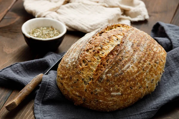 Round loaf of freshly baked sourdough bread with knife on napkin. Artisan bread with seeds on wooden table. Rustic sourdough bread.