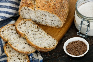 Keten havluyla dilimlenmiş çoklu tahıllı ekşi ekmek. Esnaf ekmeği, un kavanozu, ketenli kase..