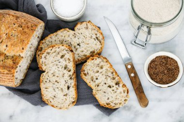 Keten havluyla dilimlenmiş çoklu tahıllı ekşi ekmek. Esnaf ekmeği, un kavanozu, ketenli kase..