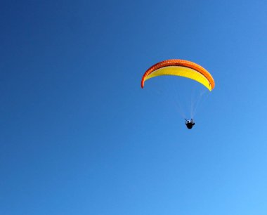 Güneşli bir günde mavi gökyüzü ile havada yamaç paraşütü yaparken canlandırıcı bir görüntü.