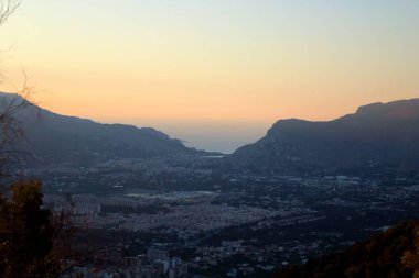 Arkasında dağlar ve deniz olan şehrin üzerindeki gün batımının canlandırıcı görüntüsü.