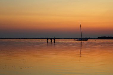 Günbatımında denize demir atmış yelkenli teknesi ve arka planda da burunlar.