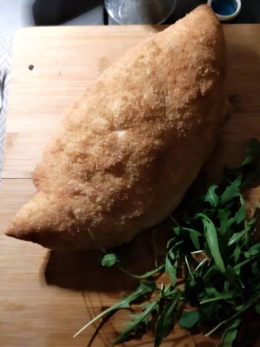 Tahta tepside roket salatalı kızarmış pizzanın canlandırıcı görüntüsü.