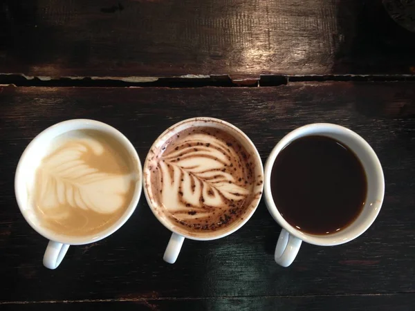 暗い茶色の木製のテーブルにブラック コーヒー カフェラテの つのカップの上から見る — ストック写真