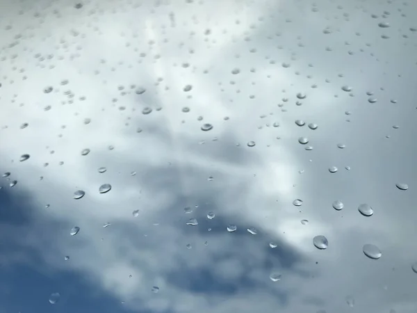 Gocce di pioggia sulla finestra di vetro trasparente e cielo bianco e blu sfocato — Foto Stock