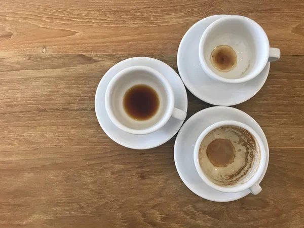 Trzy filiżanki gotowej gorącej kawy z pianką latte pozostały w filiżankach na drewnianym stole — Zdjęcie stockowe