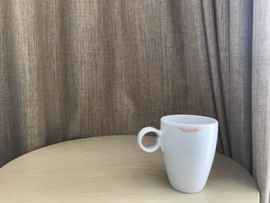 Ahşap masada kırmızı ruj izi olan beyaz seramik kahve fincanı.