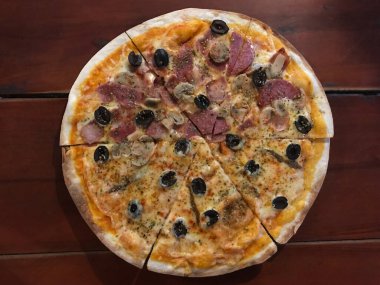 Akşam yemeğinde Küba ve Napoli pizzalarının yarısını koyu kahverengi ahşap masada görüyoruz.