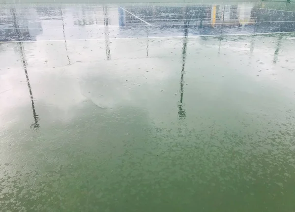 Doğal gün ışığında yağmur yağarken spot ışıklarının gölgesi boş mavi ve yeşil tenis kortunda.