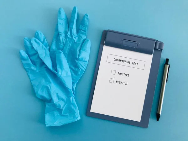 Coronavirus test çizelgesi ve gri kalemli mavi eldivenlerin boş mavi arkaplan üzerindeki negatif sonucu.