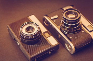 Eski kameralar masanın üzerinde. Siyah bir zemin üzerine iki vintage kameralar