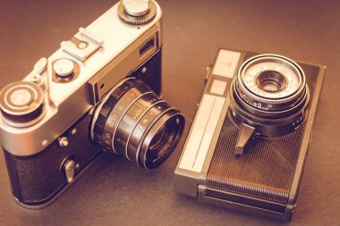 Eski kameralar masanın üzerinde. Siyah bir zemin üzerine iki vintage kameralar