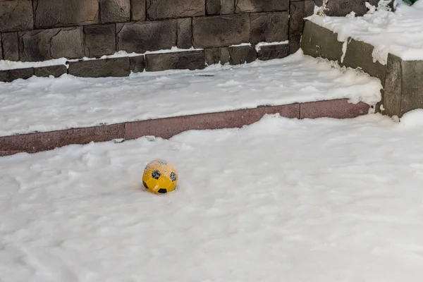 Palla gialla per bambini nella neve nel cortile vicino al portico di una casa in pietra — Foto Stock