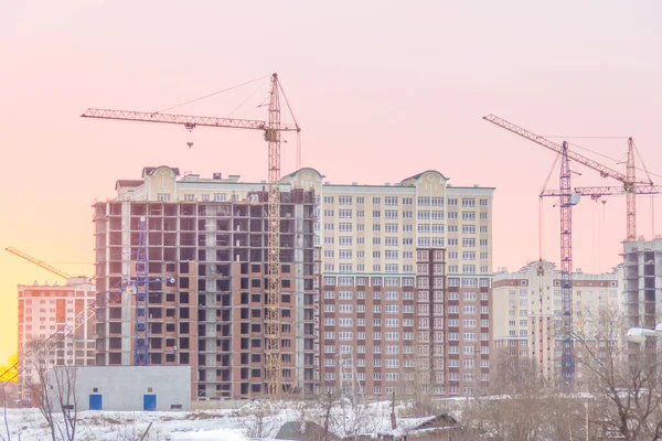 winter day, the construction of multi-story frame houses with tower cranes, the demolition of old houses to free land for construction