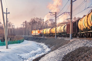 Virajdan ayrılan yük treni, sanayi bölgesinin arkasındaki ağaçlar, kış akşamı.