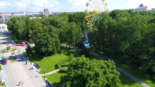 夏の暖かい雲の日に観覧車と緑の公園で市の広場 人々が静かに歩いている ドローン映像 — ストック動画