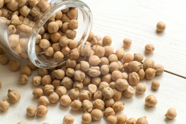 Nohut biyolojisi, beyaz arka planda devrilmiş bir bardaktan dökülen çiğ kahverengi nohut manzarası.