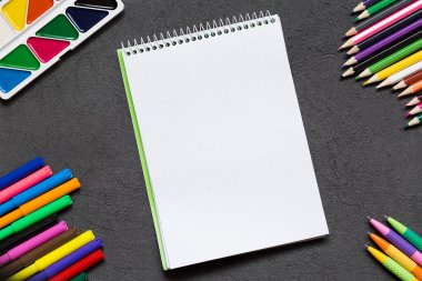 Parlak okul defteri ve siyah masanın üzerindeki çeşitli kırtasiye malzemeleri. Okul konseptine geri dön, alanı kopyala