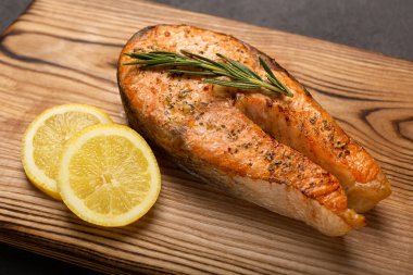 Koyu arkaplanda limonlu ızgara somon bifteği, ahşap tahtada kızarmış somon filetosu, kapat..