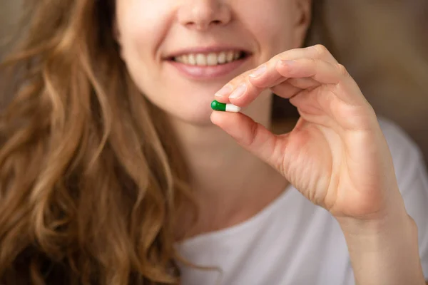 Young woman holding vitamin capsule and smiling, close up. Medicine pills or capsules in hand.