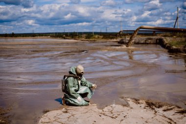 Bir bilim adamı kimyasal atık salınımından sonra su örneği alır. Solunum cihazına bağlı bir adam ve radyasyondan korunan yeşil bir giysi. Su analiz uzmanları. Maske. Ekolojik felaket.