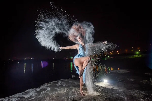 Femme rousse en robe bleue avec un décolleté profond dansant dans des nuages de farine. Une fille sur la rive de la rivière sautant éparpillant la poudre blanche . — Photo