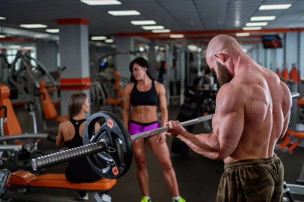 Bald man with a beard in the gym. Muscular bodybuilder guy doing barbell exercises. Strong man with a naked torso. The young athlete is preparing for weightlifting competitions.