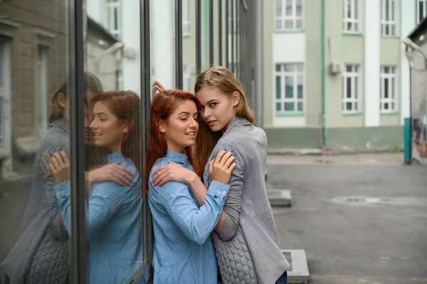 Vztahy stejného pohlaví. Portrét dvou mladých lesbiček vášnivě objímajících a stojících u zrcadlové stěny. Milující pár gayů stojící na ulici a projevující city. — Stock fotografie