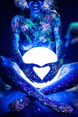 Floresan tozuyla boyanmış bir kadın küresel bir lamba tutuyor. Renkli vücut spreyiyle bir kızın bacaklarının yakınlaştırılması. Yuvarlak neon gece lambası.