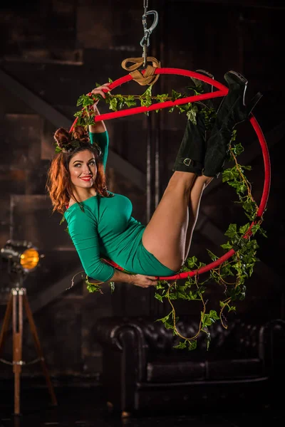 Beautiful woman gymnast performs tricks on an aerial hoop. A girl dressed as poison ivy cosplay on a batman. Circus acrobat on the ring.