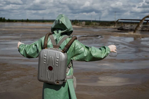 Un ambientalista masculino con traje protector verde y máscara de gas toma una muestra de agua en un lago contaminado. Residuos de la producción. Un científico hace un estudio toxicológico de residuos tóxicos . —  Fotos de Stock